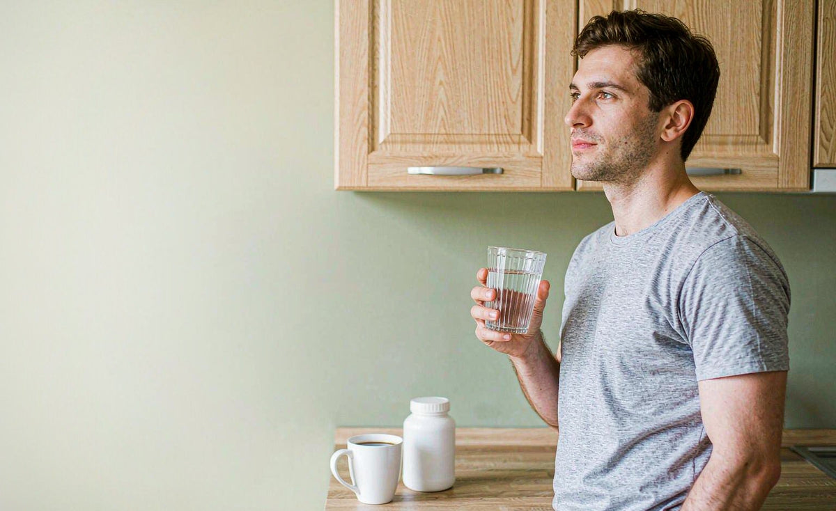 Man at a kitchen counter with a glass of water and a supplement bottle